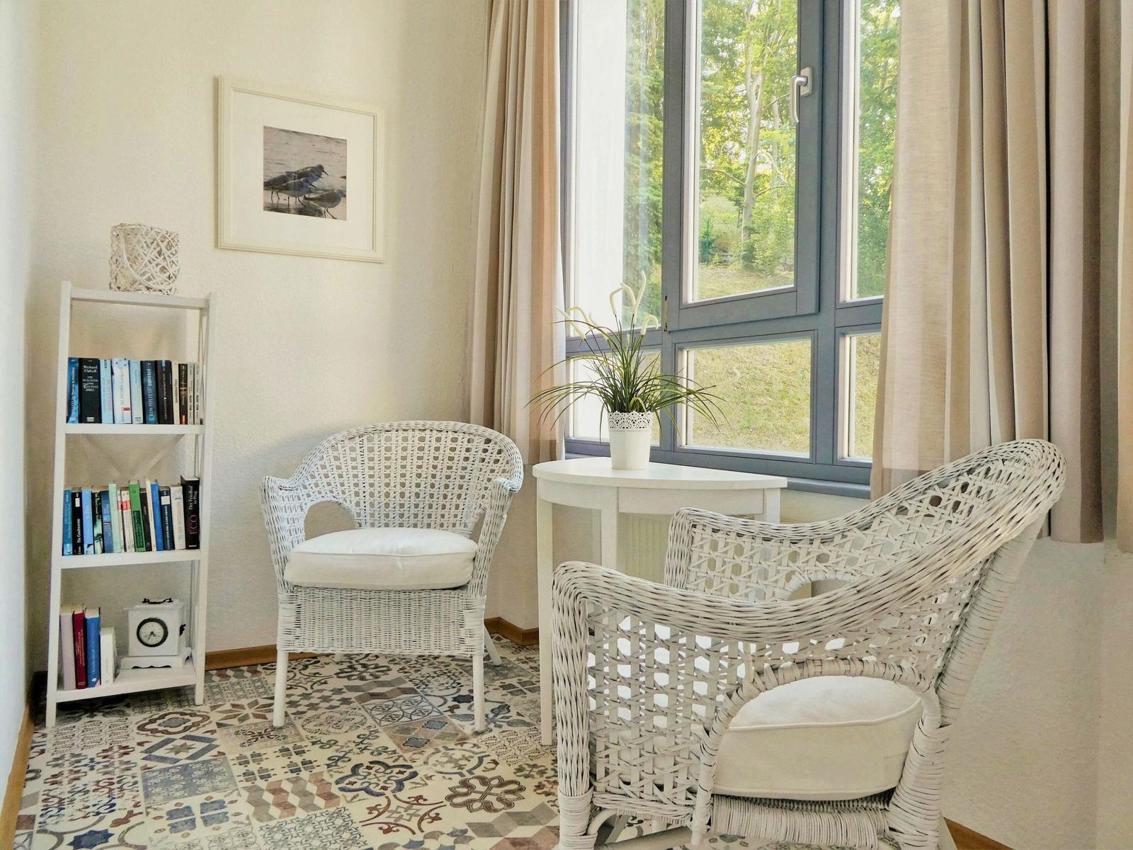 Zwei weiße Rattan-Stühle stehen vor einem großen Fenster mit Blick auf Grün.