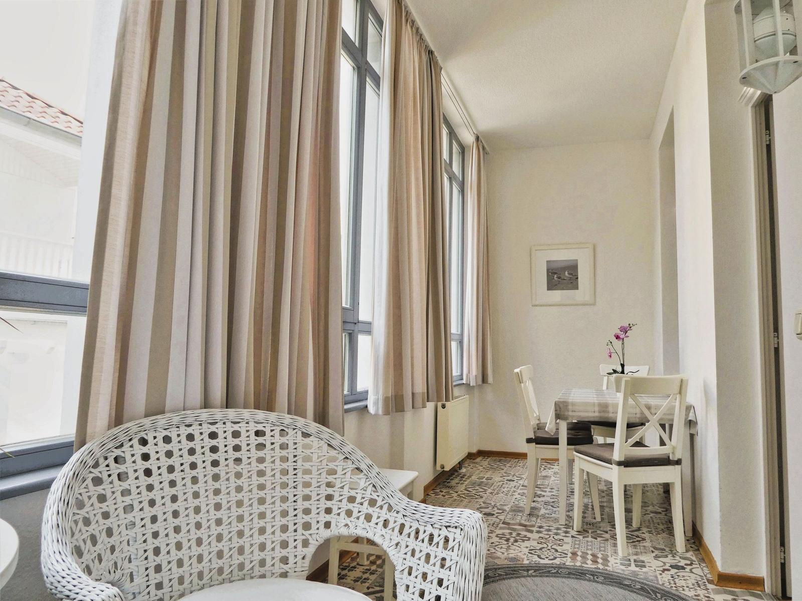 Raum mit Sitzgelegenheit, Esstisch und Fenstern mit Vorhängen.