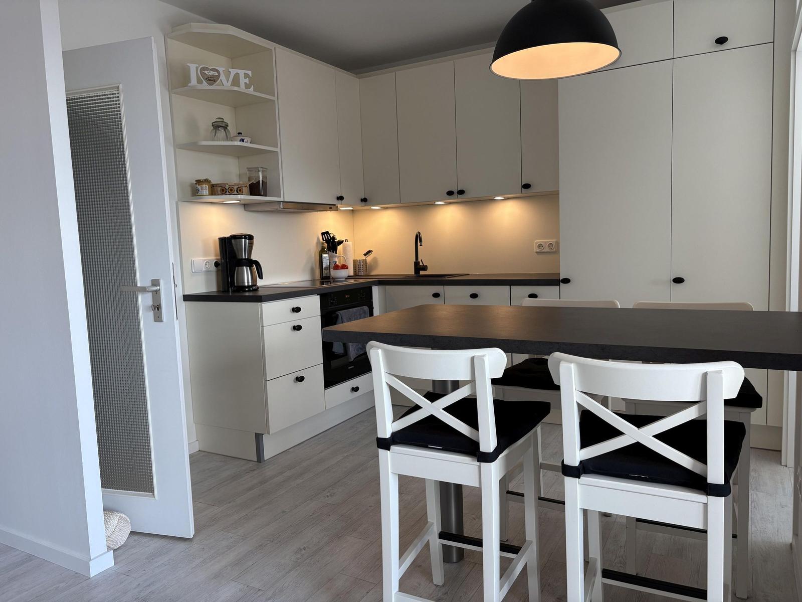 Küche mit Essbereich, weißen Schränken und schwarzer Arbeitsplatte.
