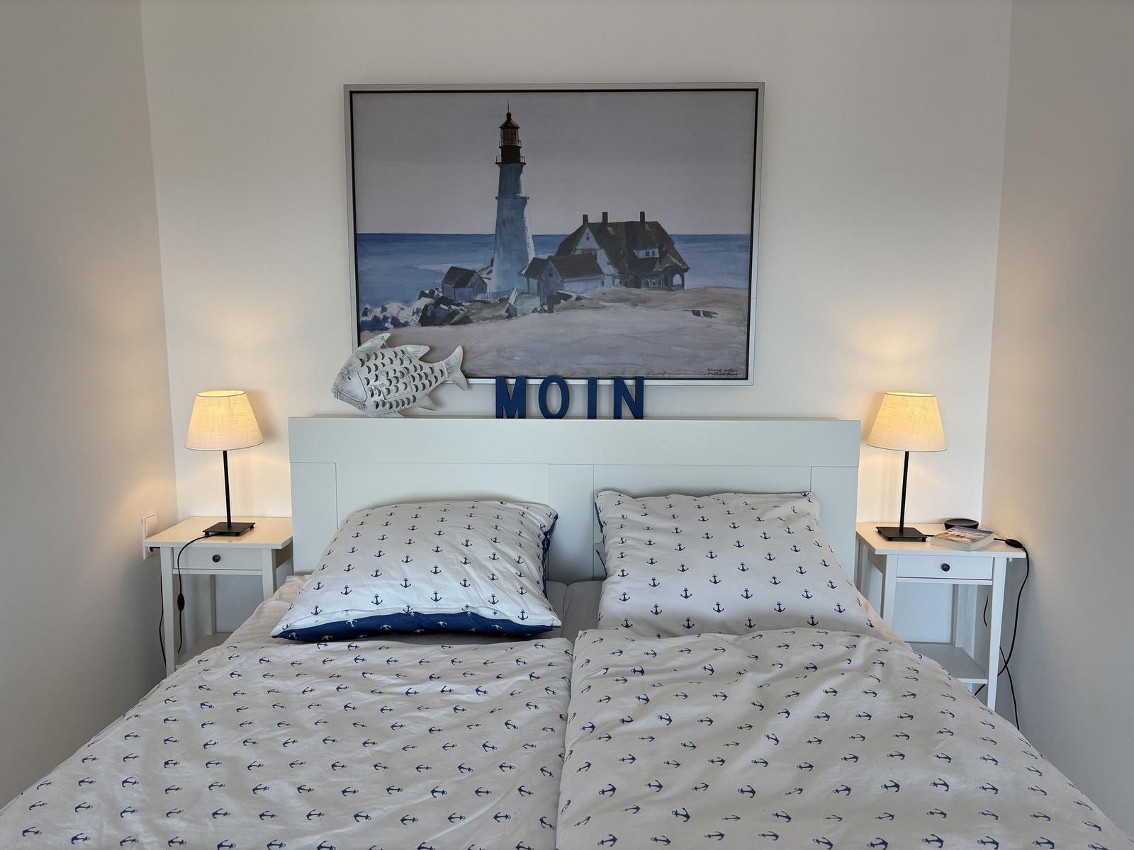 Schlafzimmer mit Bett, zwei Nachttischen und Wandbild mit Leuchtturm.
