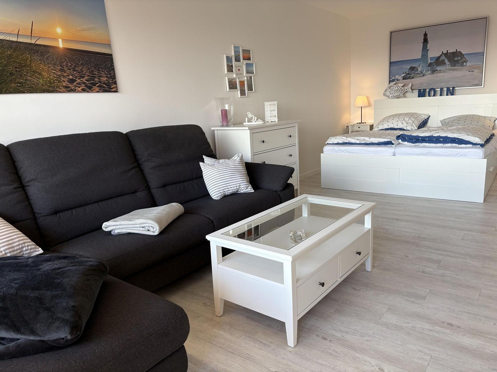 Wohnbereich mit Sofa, Couchtisch und Schlafzimmer mit Bett und Wandbild.