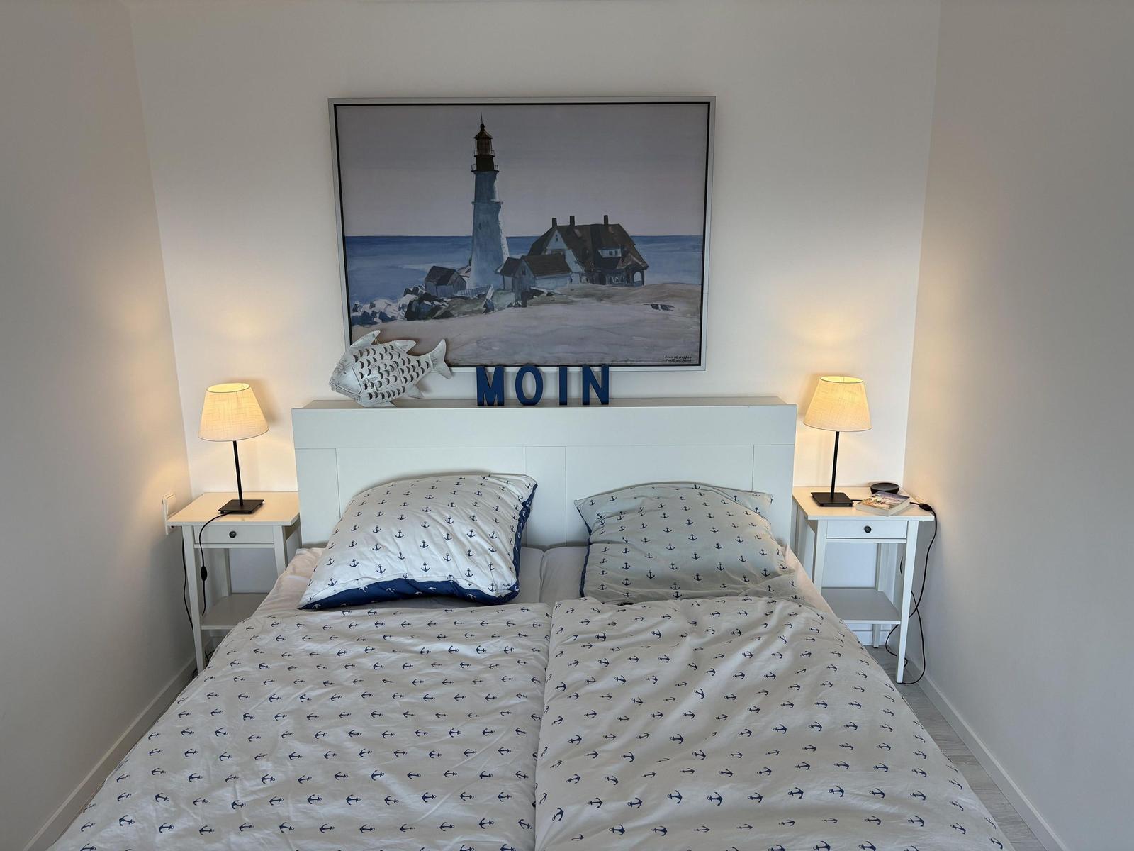 Schlafzimmer mit Bett, Nachttischen und Wandbild mit Leuchtturm.