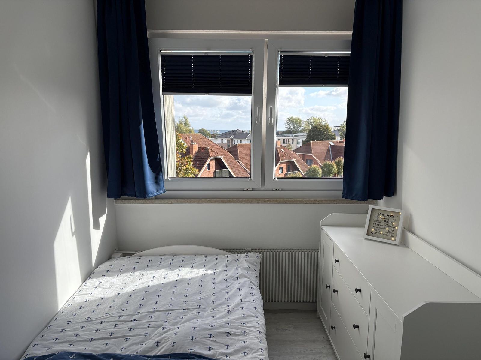 Ein Schlafzimmer mit Blick auf Dächer und See. Bett, Schrank und Fenster sind sichtbar.
