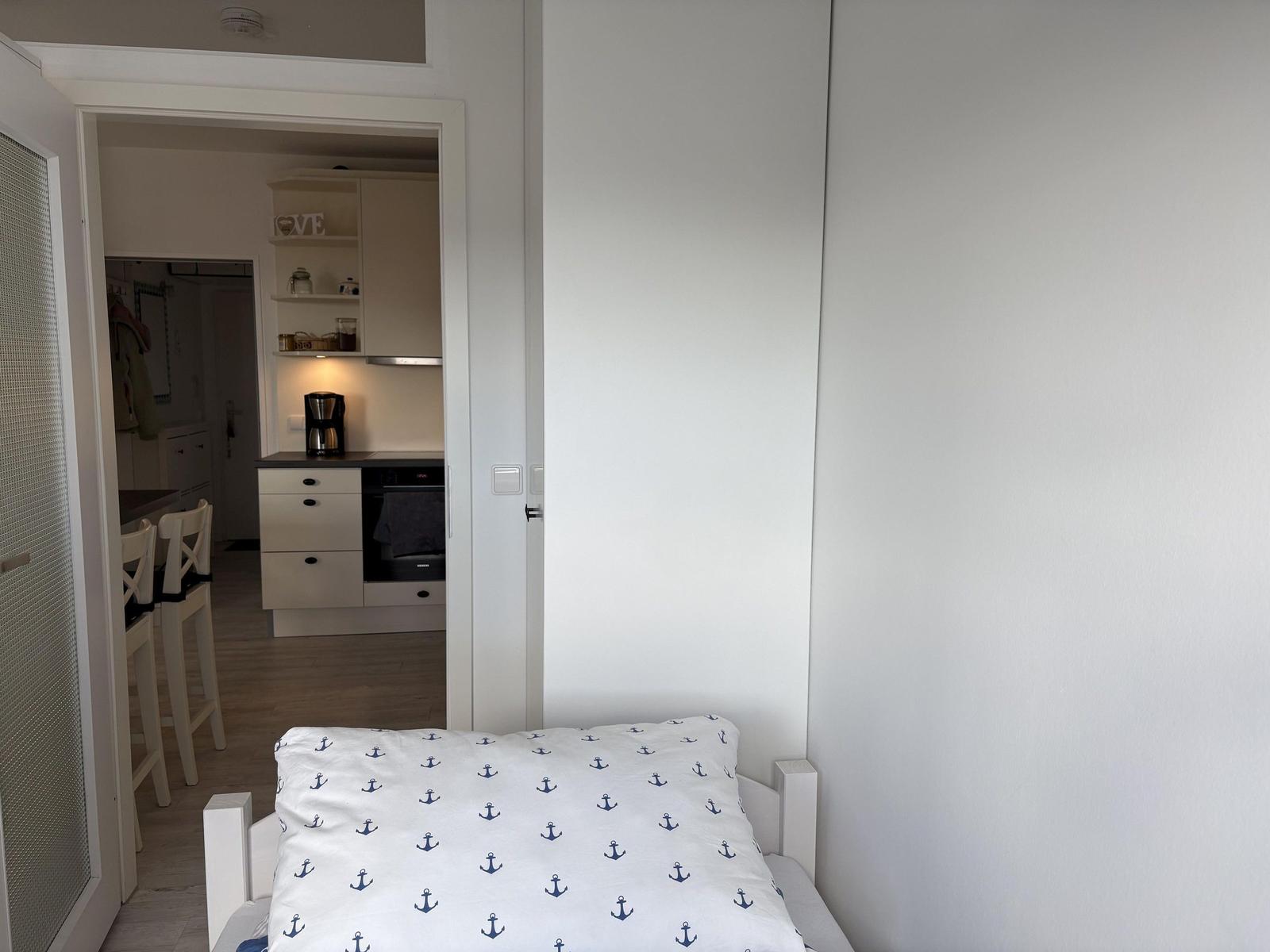 Schlafzimmer mit Bett und Blick in die Küche.