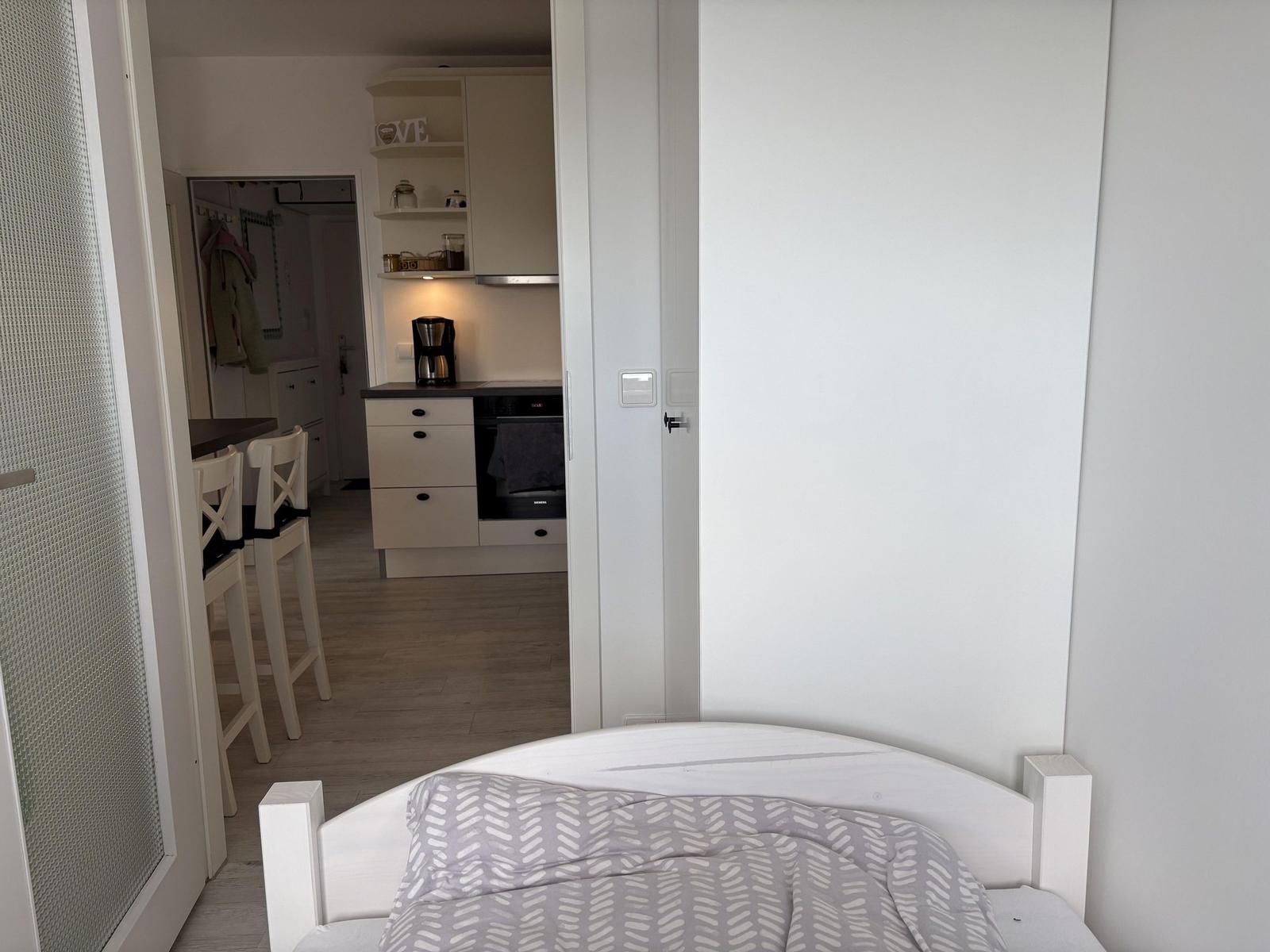 Schlafzimmer mit Bett und Blick in die Küche mit Esstisch.