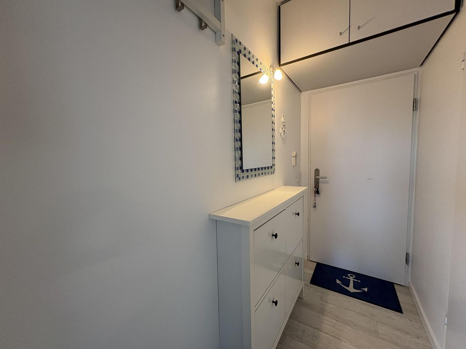 Eingangsbereich mit Schuhschrank, Spiegel und Tür mit Ankermatte.
