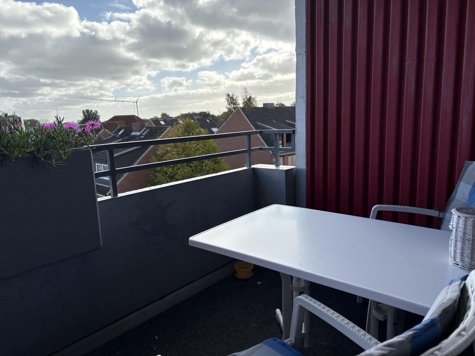 Terrasse mit Tisch und Stühlen, Blick auf Dächer und Himmel.