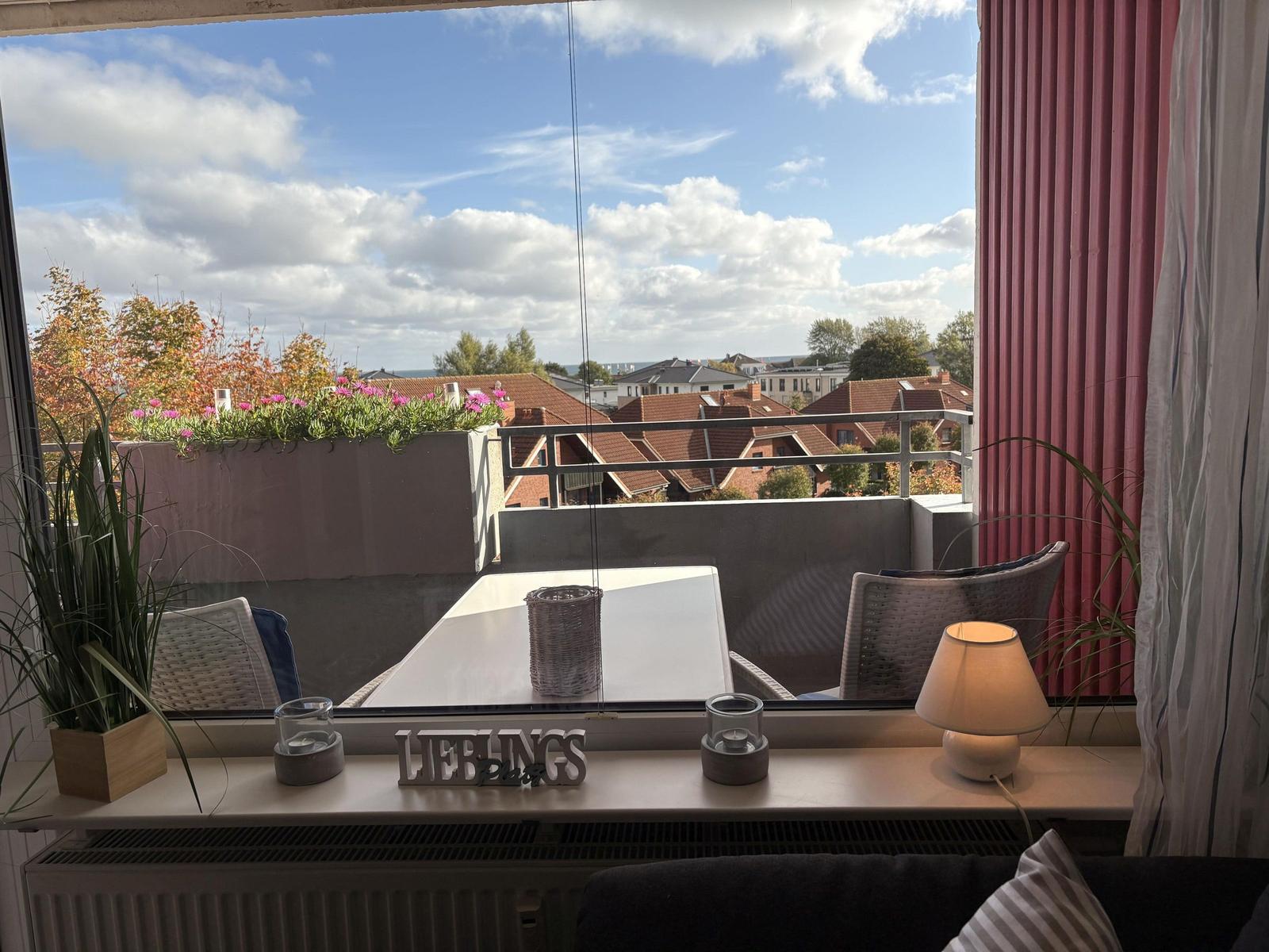 Balkon mit Tisch, Stühlen und Blick auf Dächer und Meer.