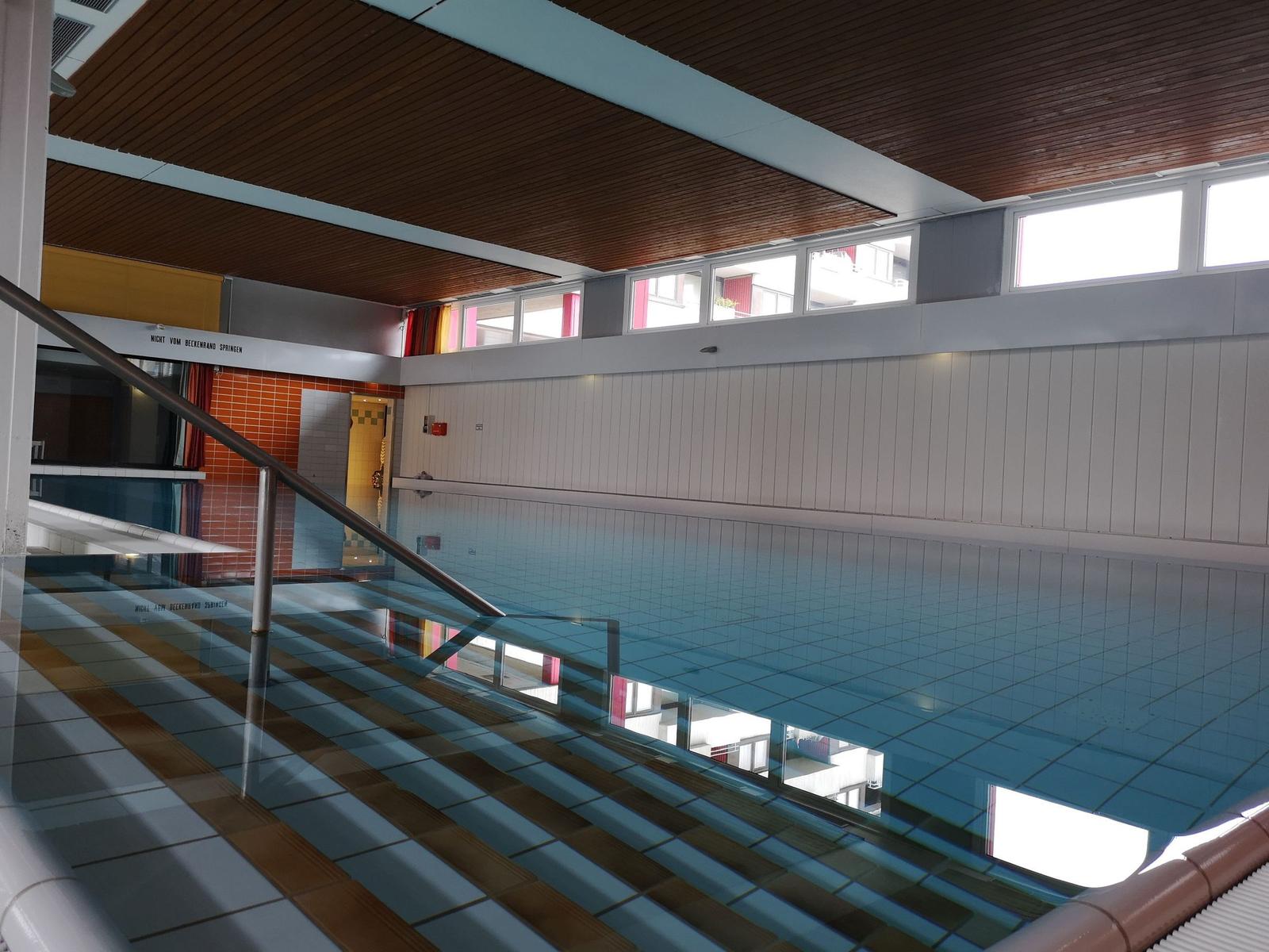 Großer Innenpool mit Glasgeländer und Holzdecke.