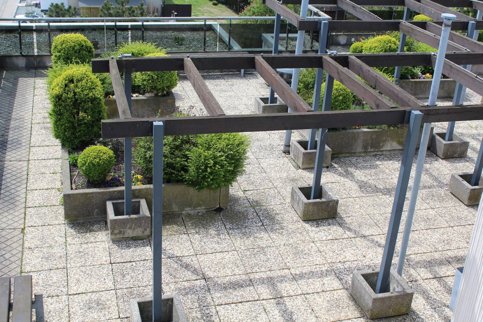 Terrasse mit Holzgestell, Pflanzen und Betonblöcken.