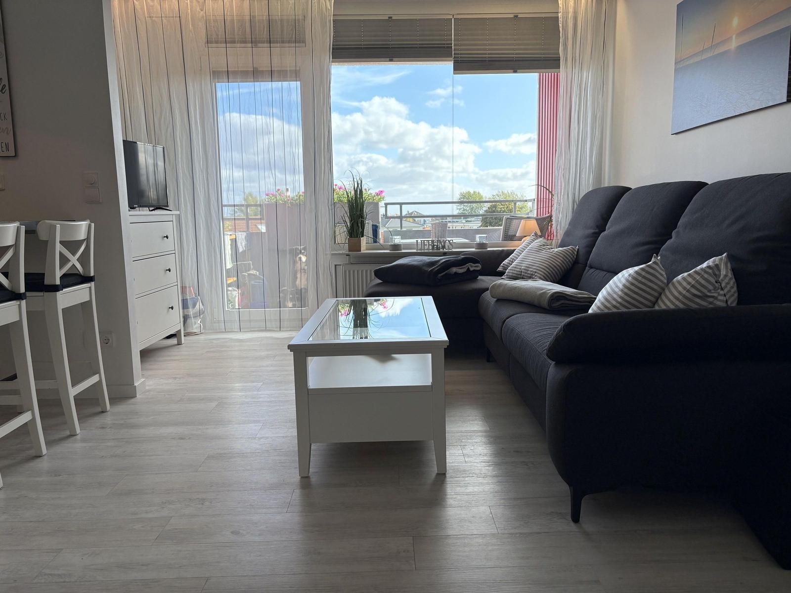 Wohnzimmer mit Sofa, Glas-Tisch und Balkonblick.