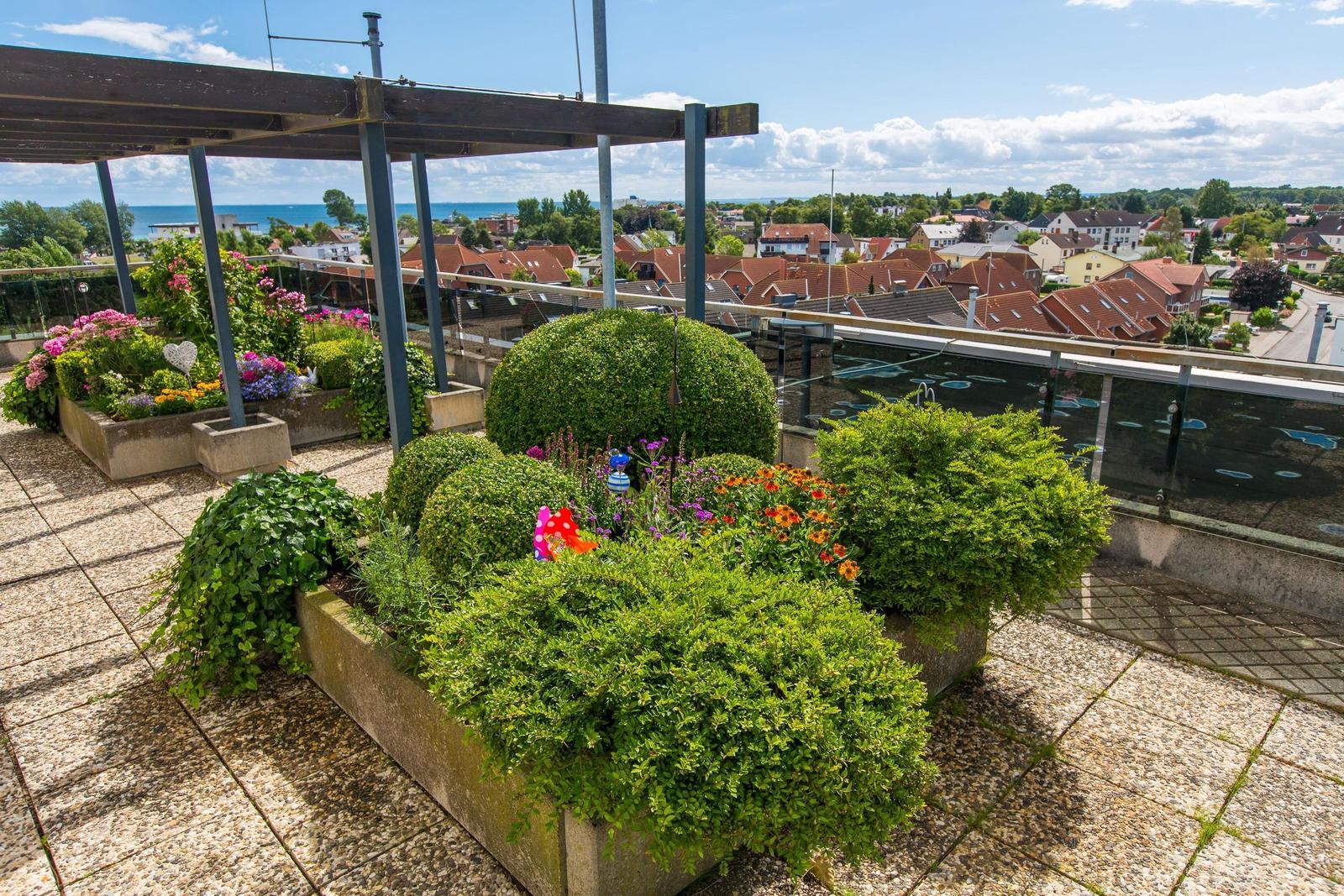 Terrasse mit Blumenbeeten und Blick auf Stadt und Meer.