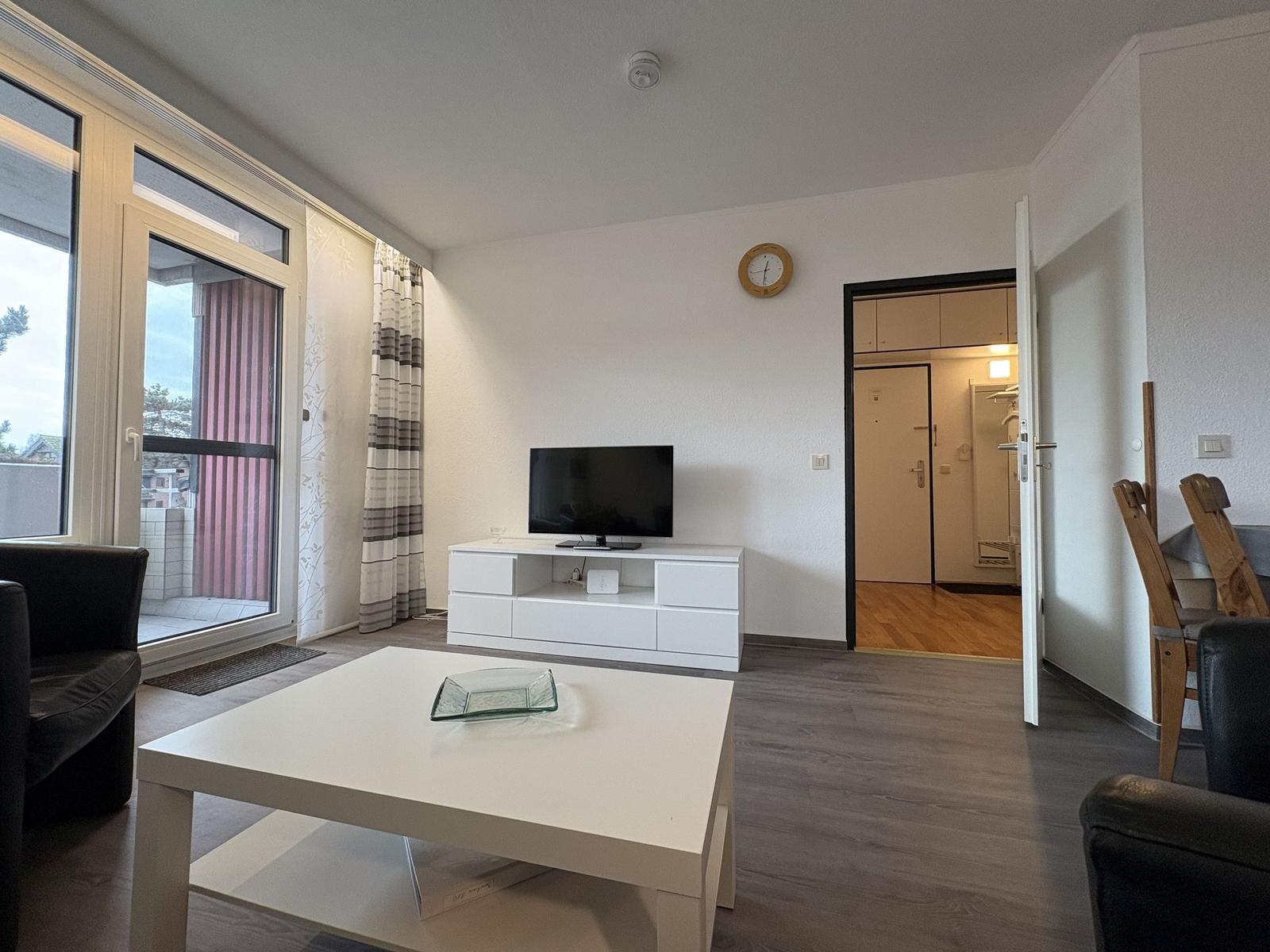 Wohnzimmer mit TV, Couch und Balkonzugang.