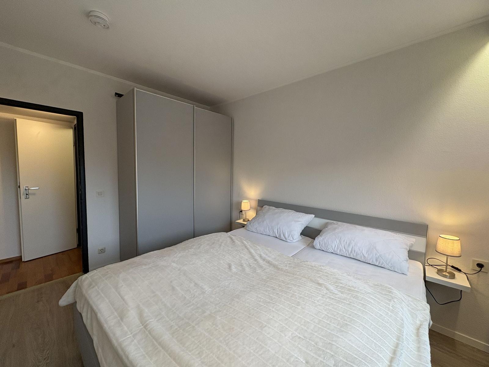 Schlafzimmer mit Doppelbett, Nachttischen und Schrank. Tür führt in angrenzenden Raum.