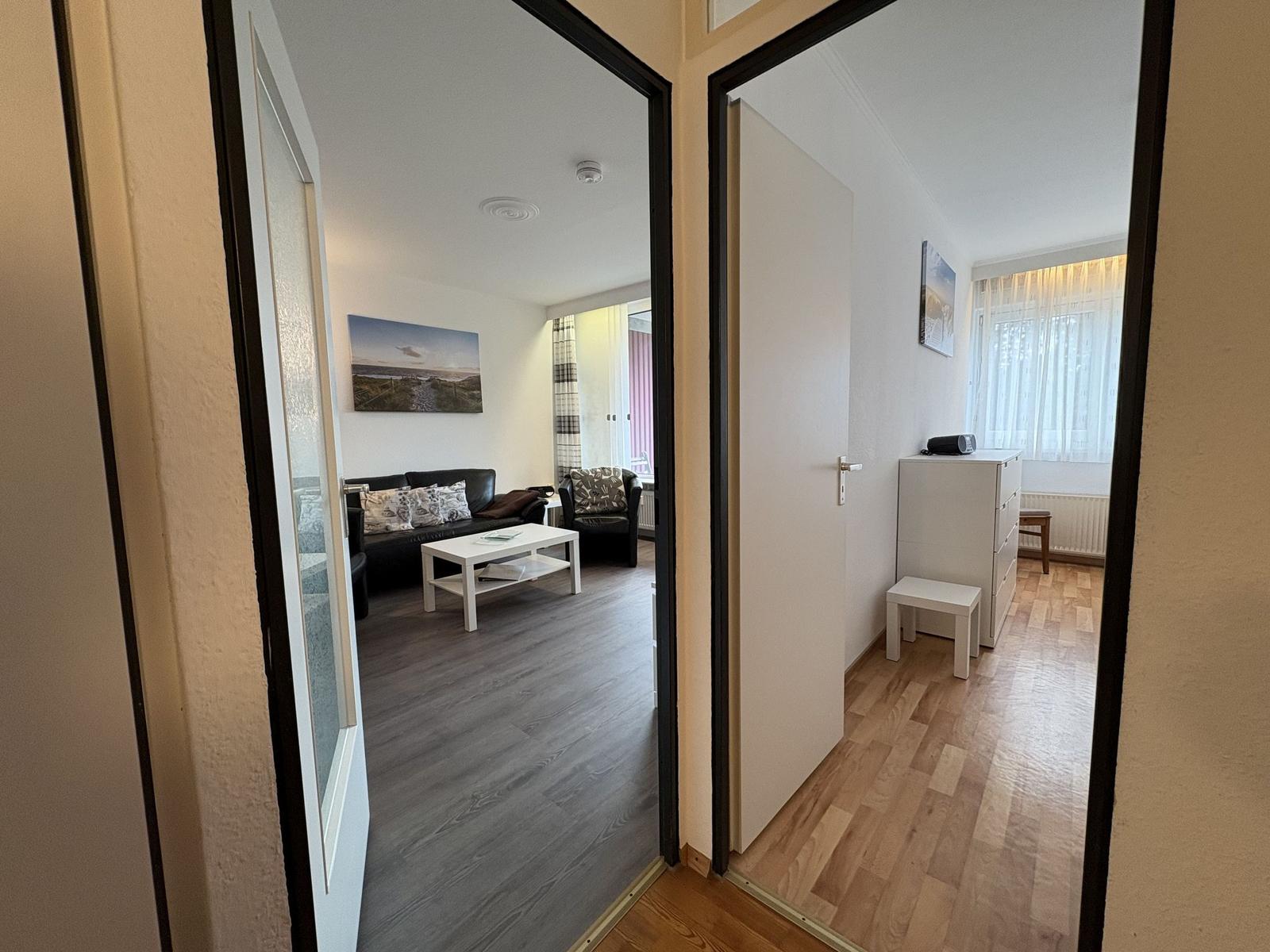 Zwei Räume sind sichtbar: ein Wohnbereich mit Sofa und ein Schlafzimmer mit Schrank.