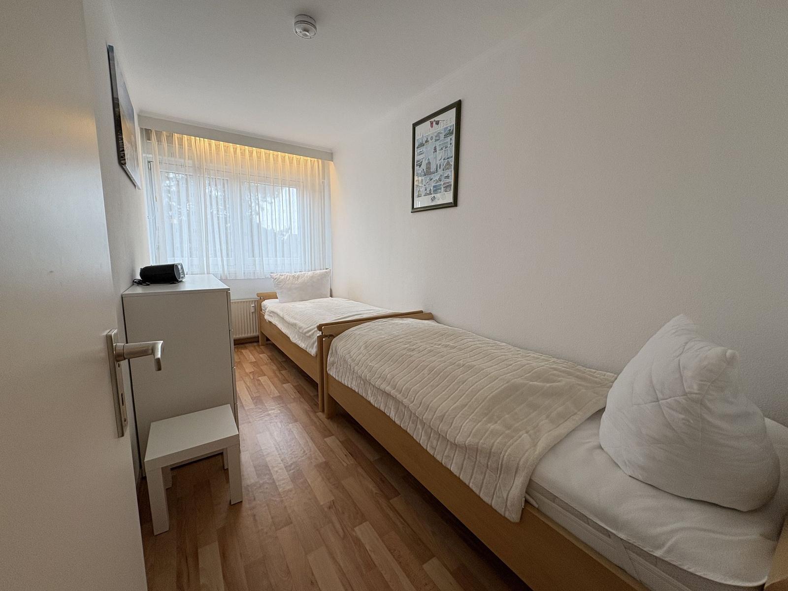 Zimmer mit zwei Einzelbetten, Holzboden und Fenster mit Vorhängen.