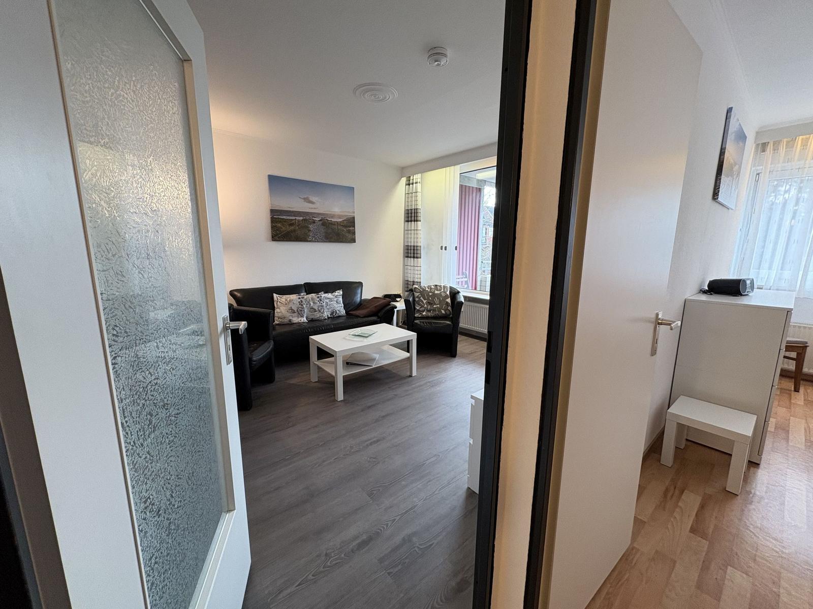 Wohnzimmer mit Sofa, Sessel und Couchtisch. Fenster mit Vorhängen.