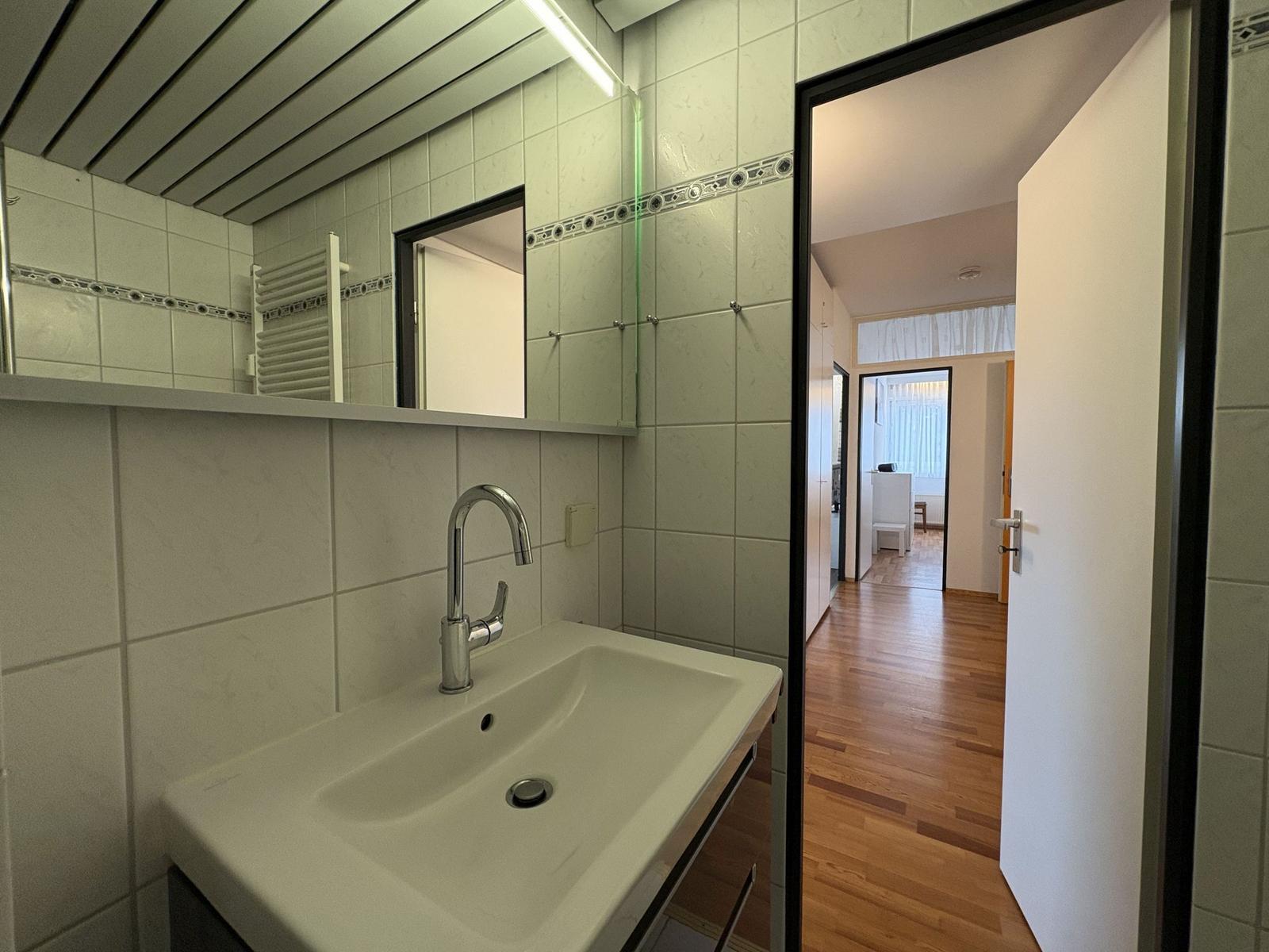 Badezimmer mit Waschbecken und Spiegel. Durchgang zur Wohnung.