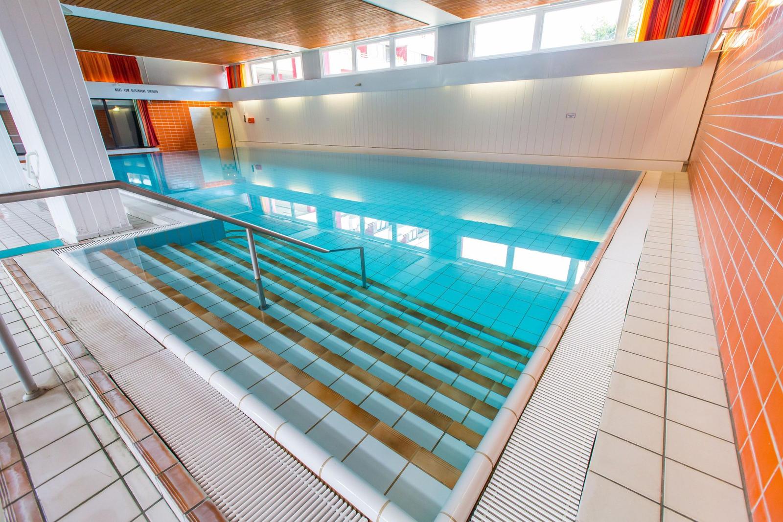 Innenpool mit Treppe und Holzdecke. Wandverkleidung aus weißen und orangefarbenen Fliesen.