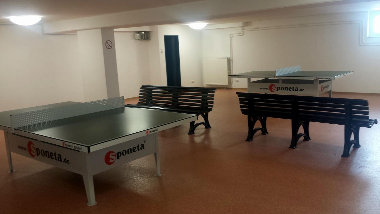 Zwei Tischtennisplatten mit Sitzbänken in einem hellen Raum mit Bodenbelag.