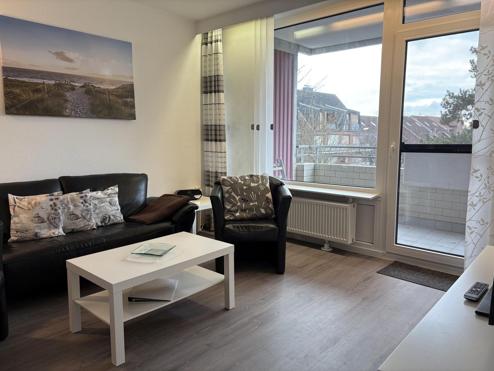 Wohnzimmer mit Sofa, Sessel und Blick auf Balkon