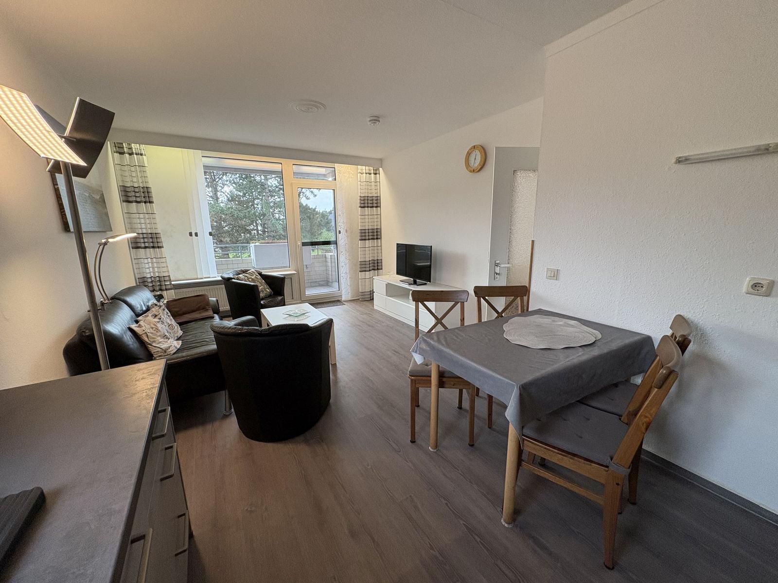 Wohn- und Essbereich mit Sofa, Tisch und Stühlen. Fenster mit Blick auf Balkon.