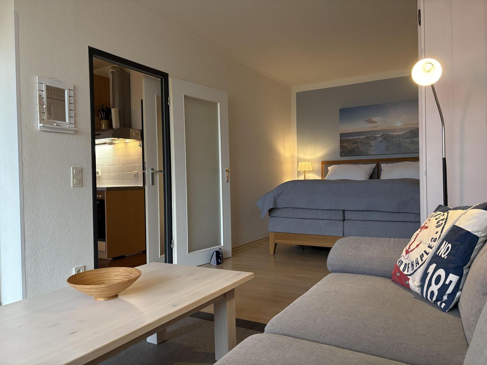 Wohnung mit Schlafzimmer, Küche und Sofa. Bett mit Kissen und Wandbild.