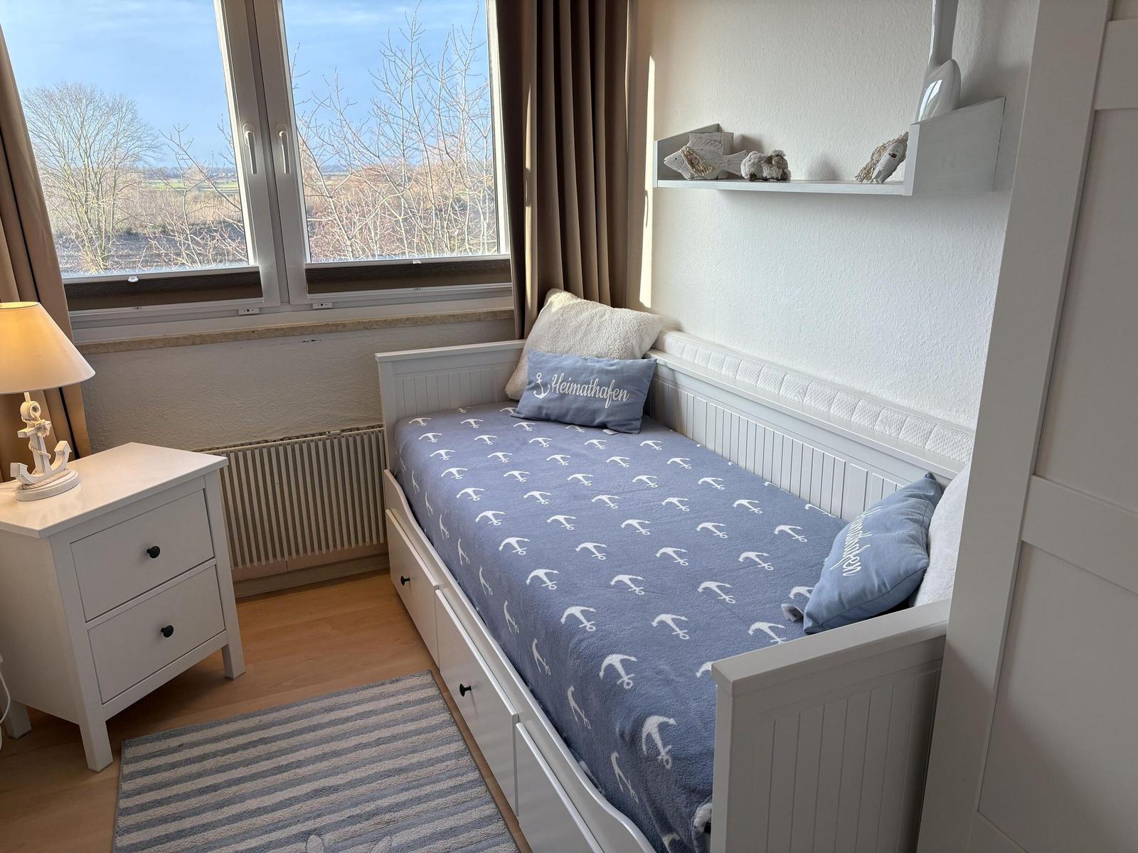 Ein Schlafzimmer mit Bett, Nachttisch und Fensterblick auf Landschaft.