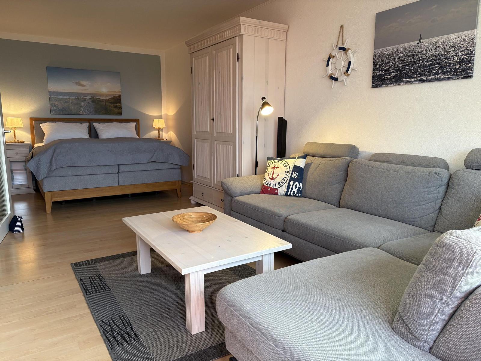 Ein Wohnzimmer mit Sofa und Bett. An der Wand hängt ein Segelbootbild.