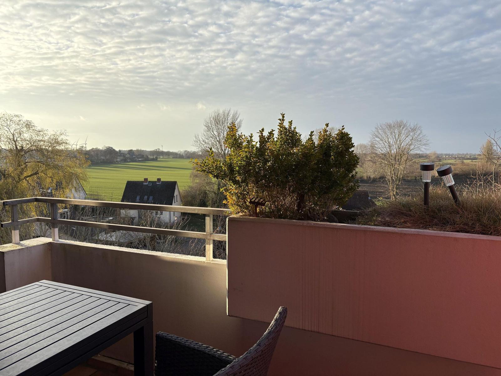 Terrasse mit Tisch und Stuhl. Blick auf grüne Wiesen und Häuser.