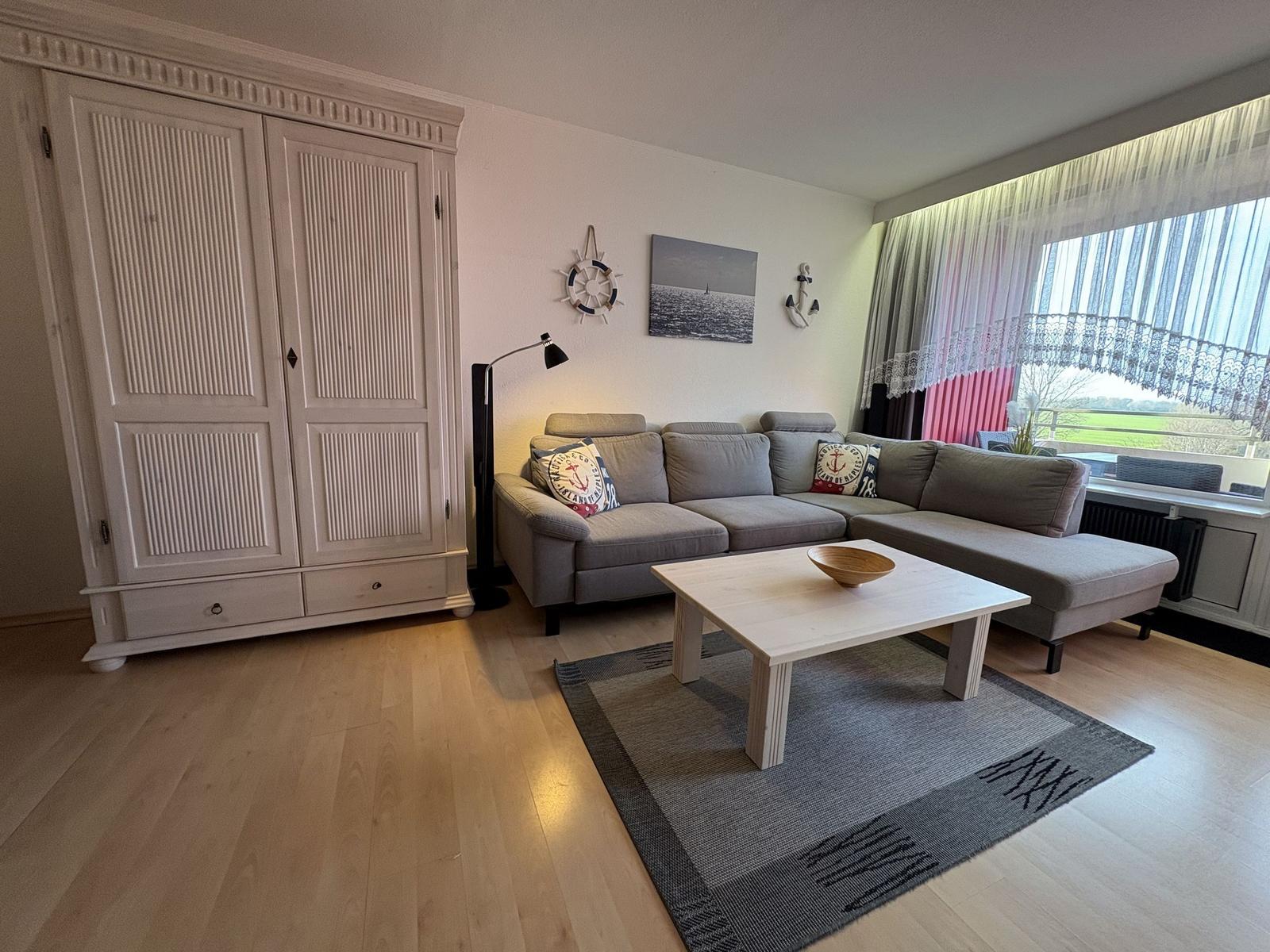 Wohnzimmer mit Sofa, Tisch und Kleiderschrank. Fenster mit Vorhängen.