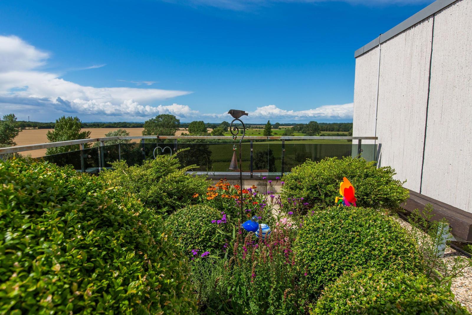 Terrasse mit Blumenbeet und Blick auf Felder und Himmel