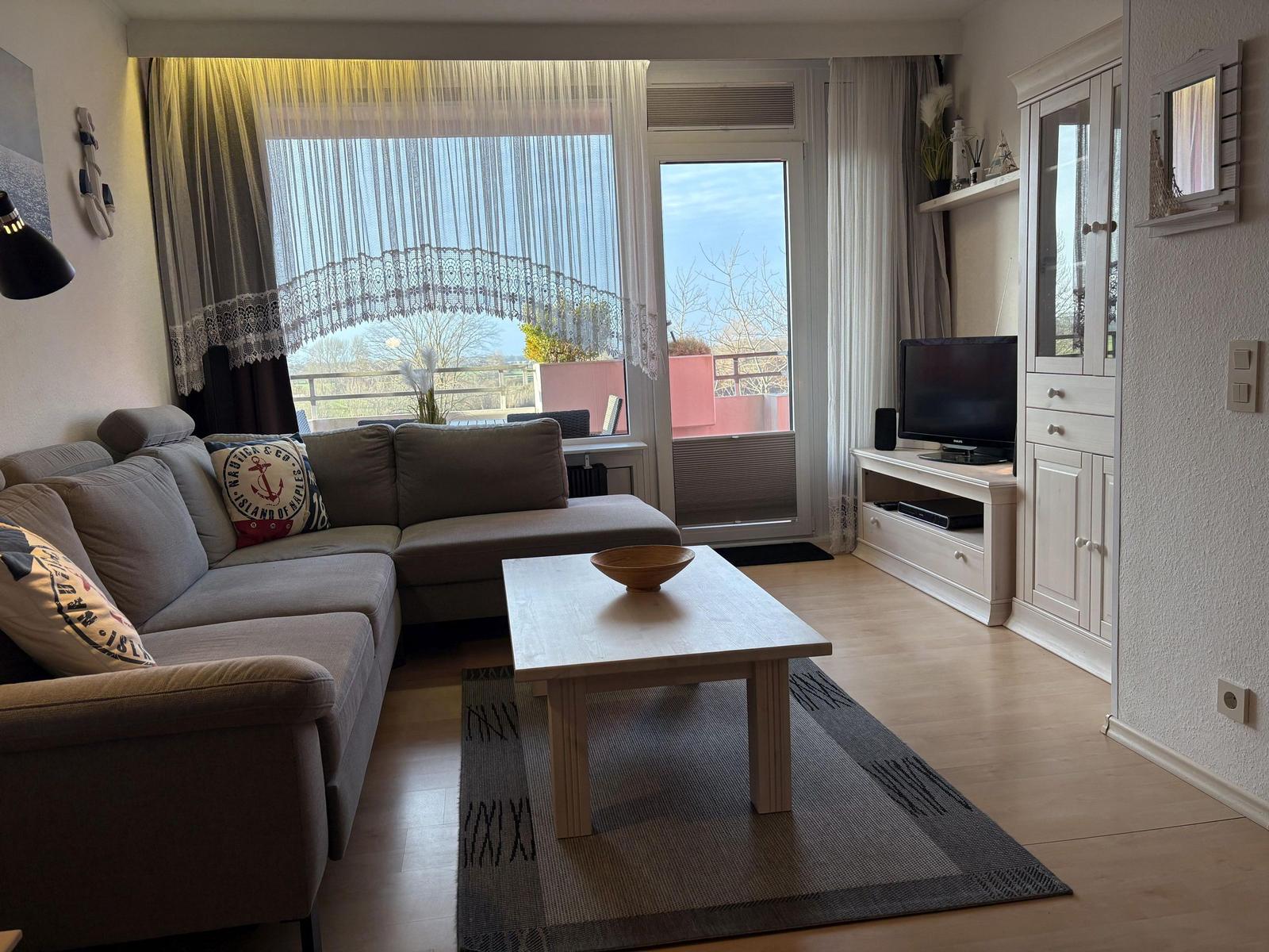 Wohnzimmer mit Sofa, Couchtisch und TV. Balkon mit Blick.