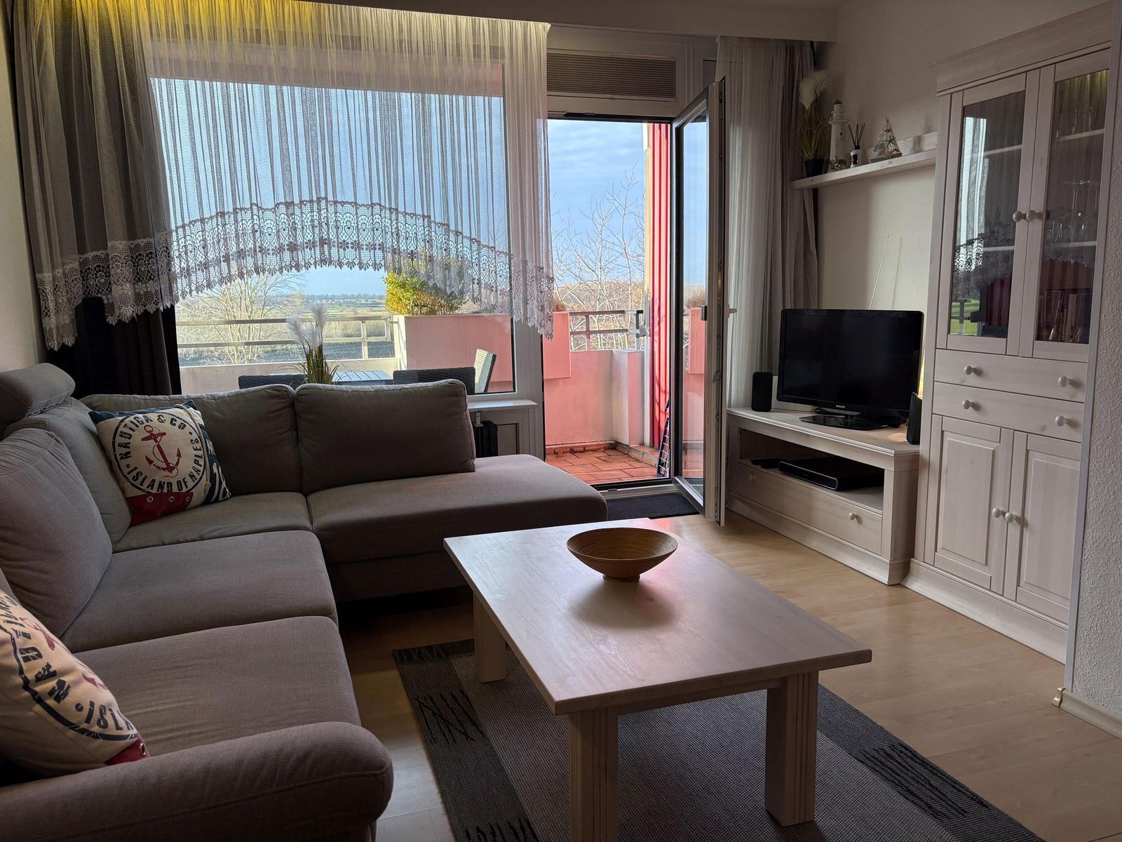 Wohnzimmer mit Sofa, Couchtisch und TV. Balkon mit Blick auf Landschaft.