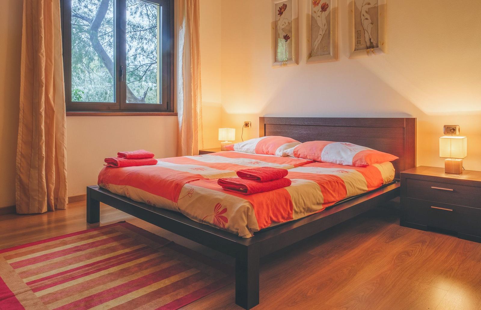 Bedroom with bed, nightstands, and window overlooking trees.