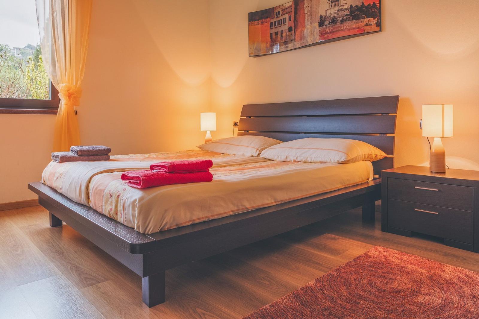 A bedroom with a bed, nightstand, and window. Towels are on the bed.
