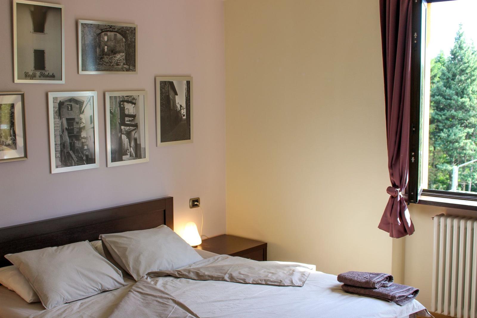 Bedroom with bed, wall pictures, and window with view of trees.