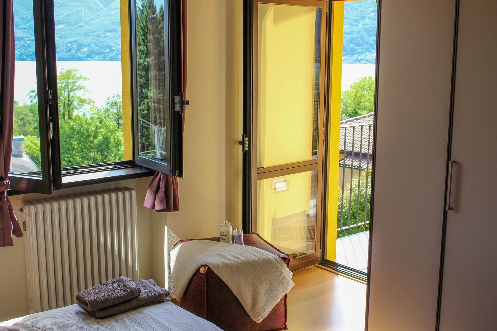 Room with view of lake and mountains, balcony, bed and radiator.