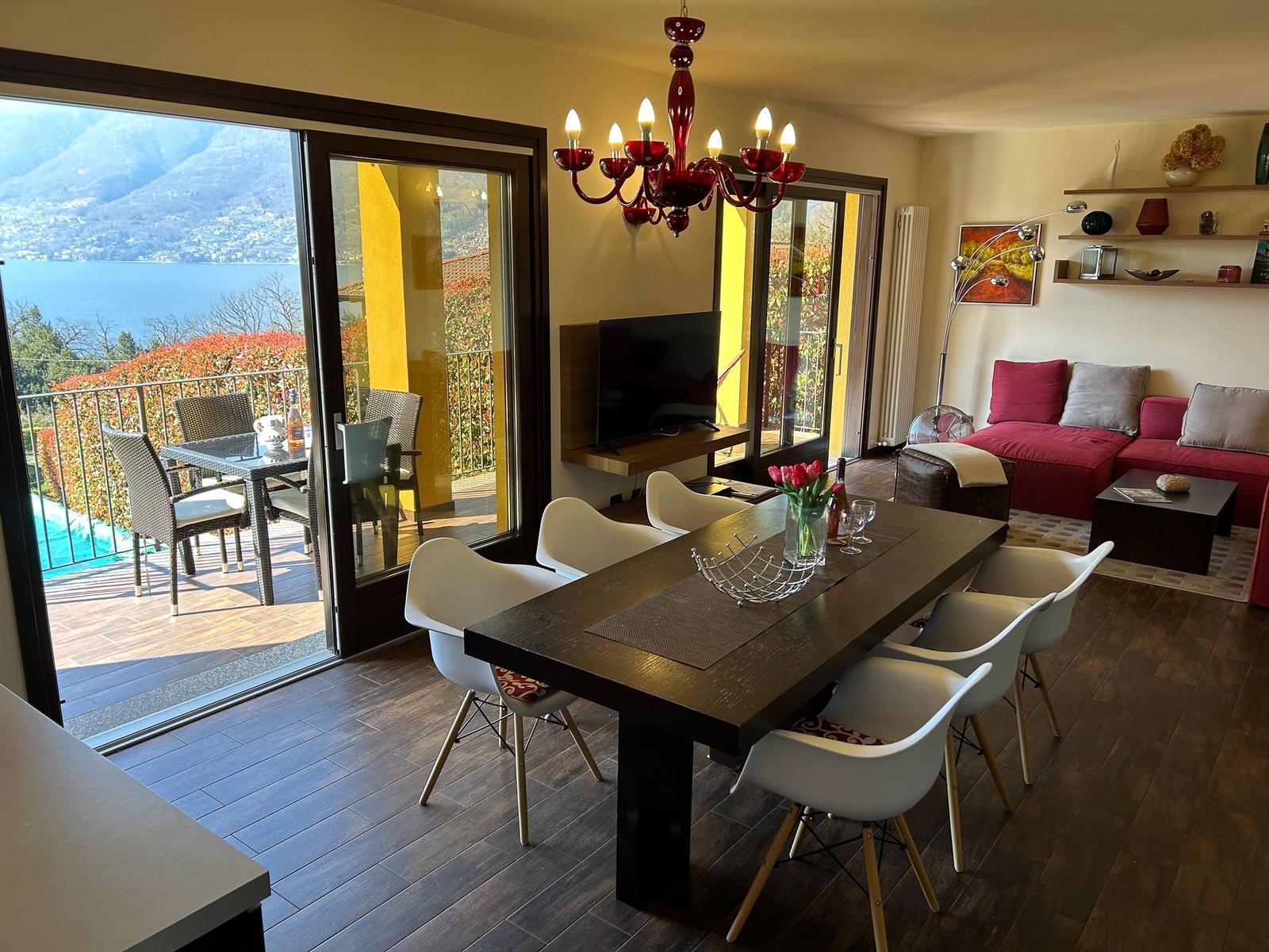 Dining room with lake and mountain view. Living area with red sofa.