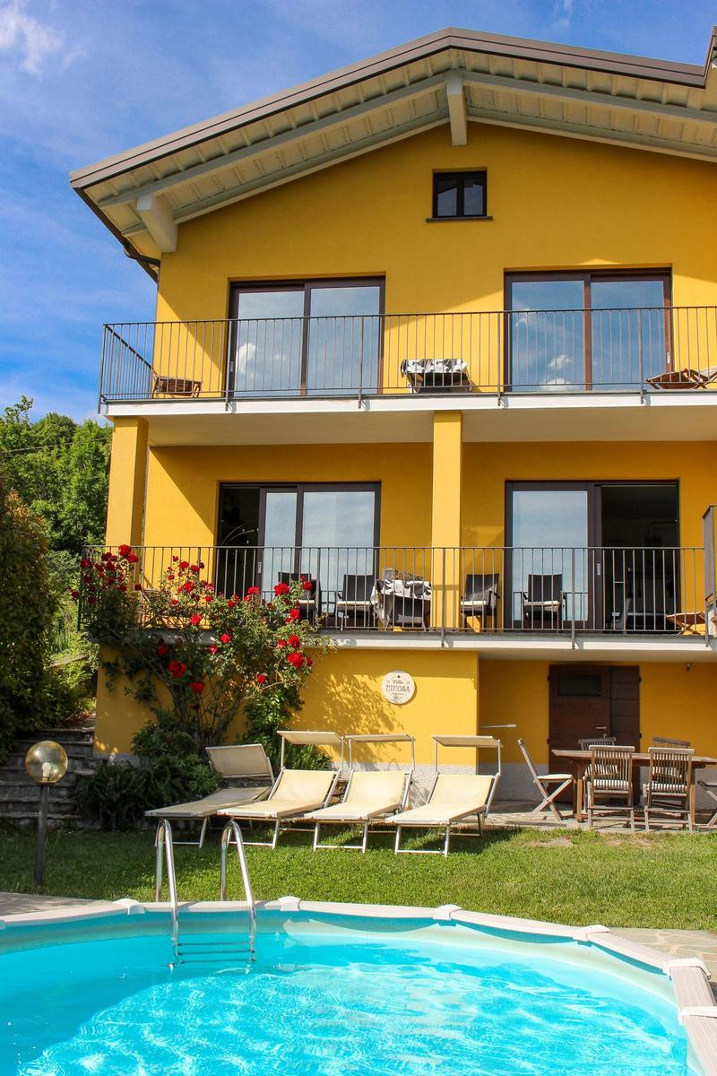 Yellow house with pool, sun loungers, and balconies. Red roses on the wall.