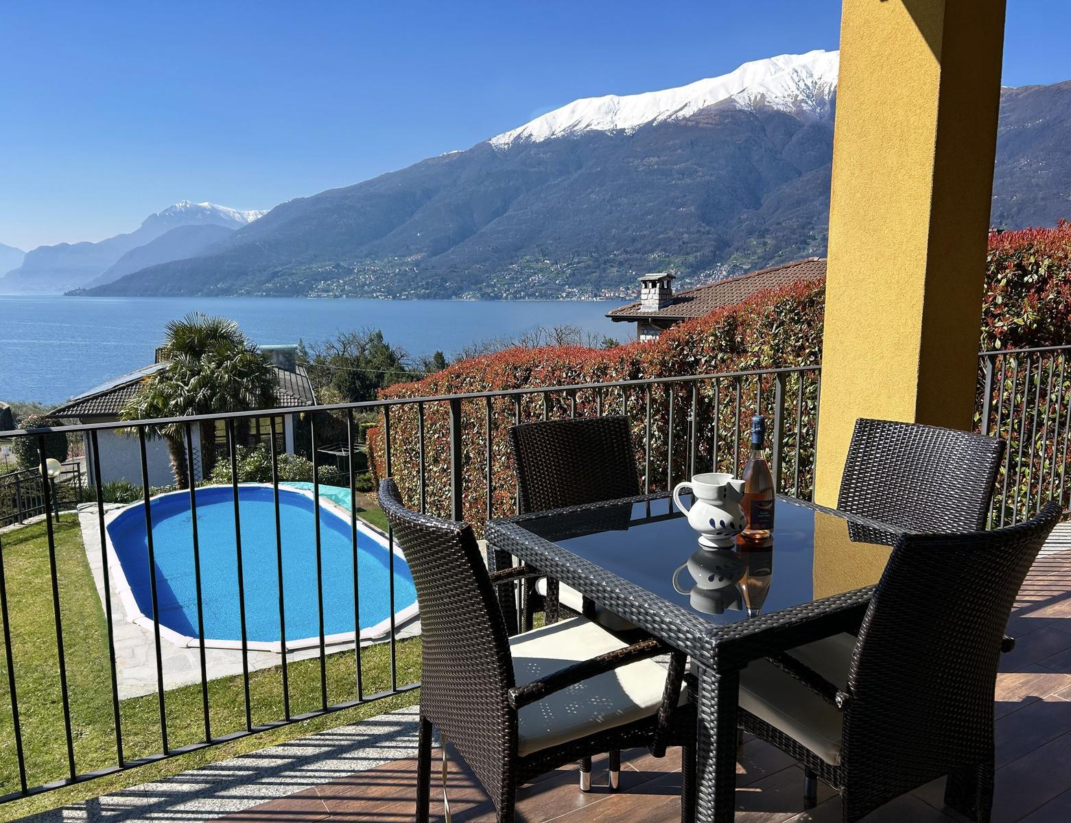 Terrace with table and chairs, view of pool and mountain lake.