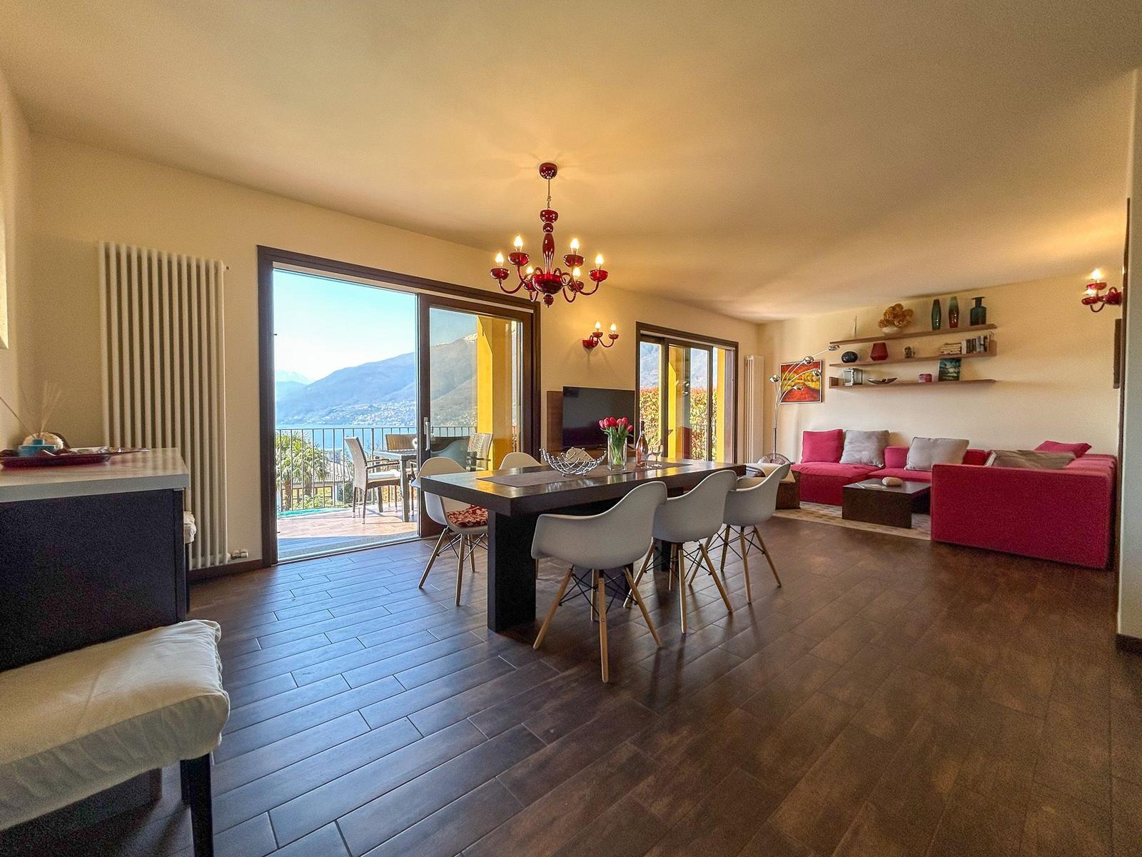 Living and dining area with balcony, red sofa, and dining table with chairs.