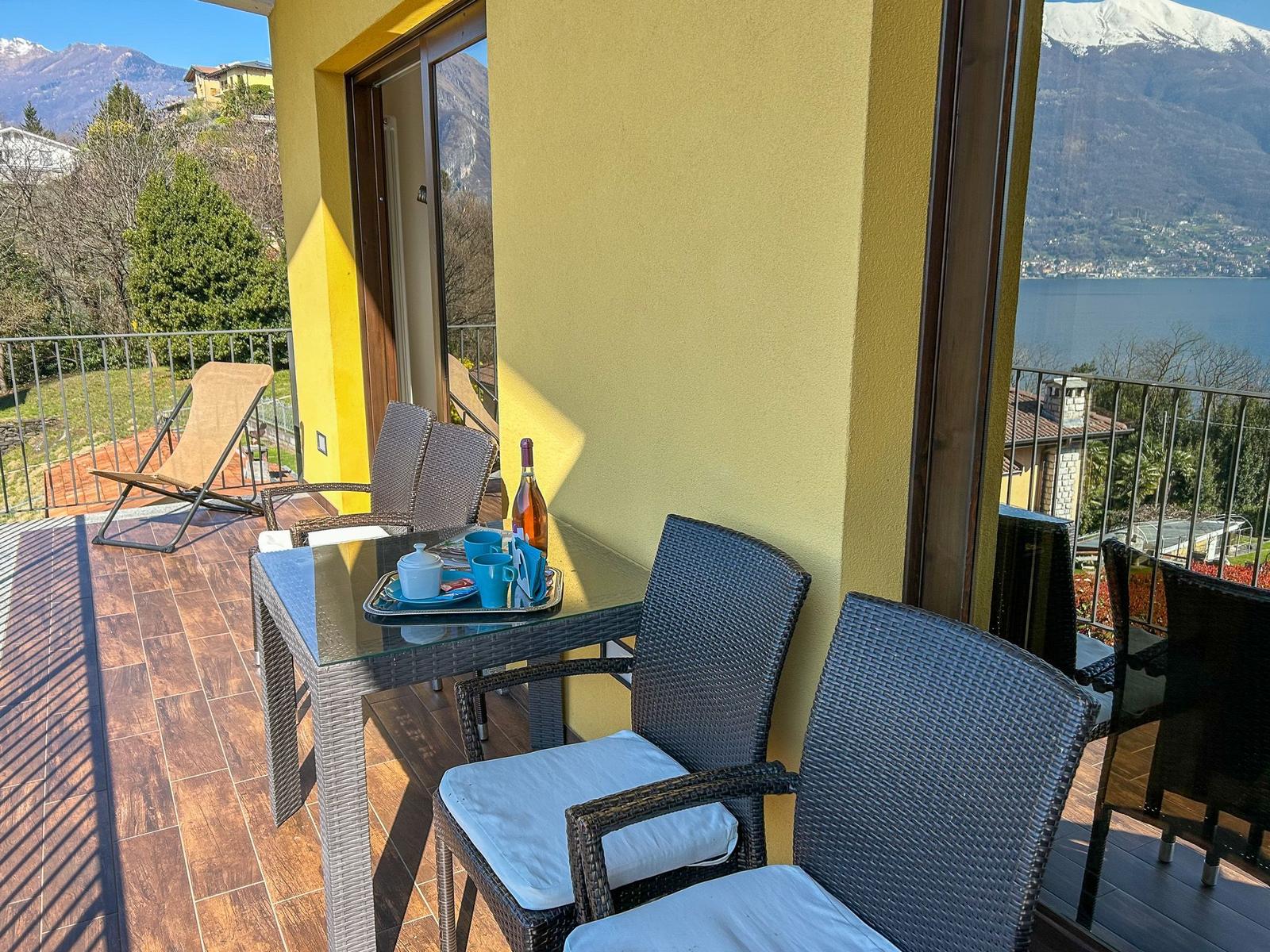 Terrasse mit Tisch, Stühlen und Blick auf See und Berge.