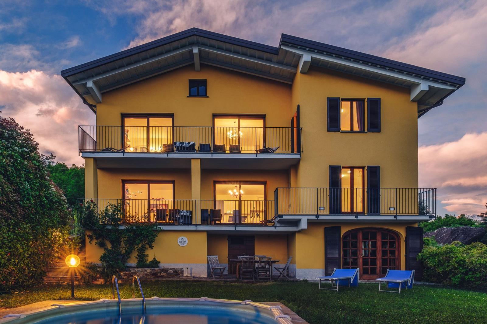 Ein gelbes Haus mit Balkonen und Pool im Garten bei Sonnenuntergang.