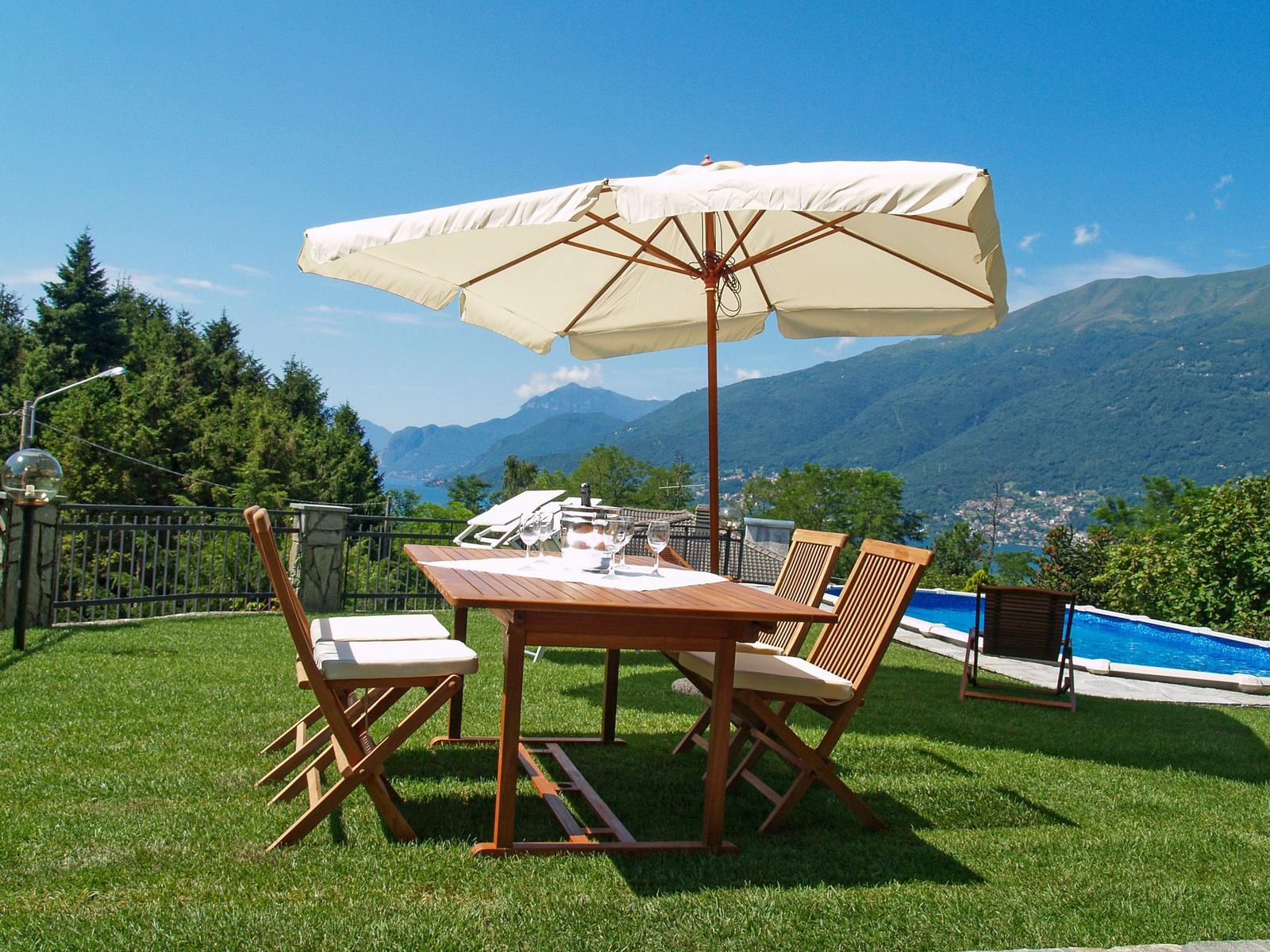 Terrasse mit Tisch, Stühlen und Sonnenschirm. Blick auf Pool und Berglandschaft.
