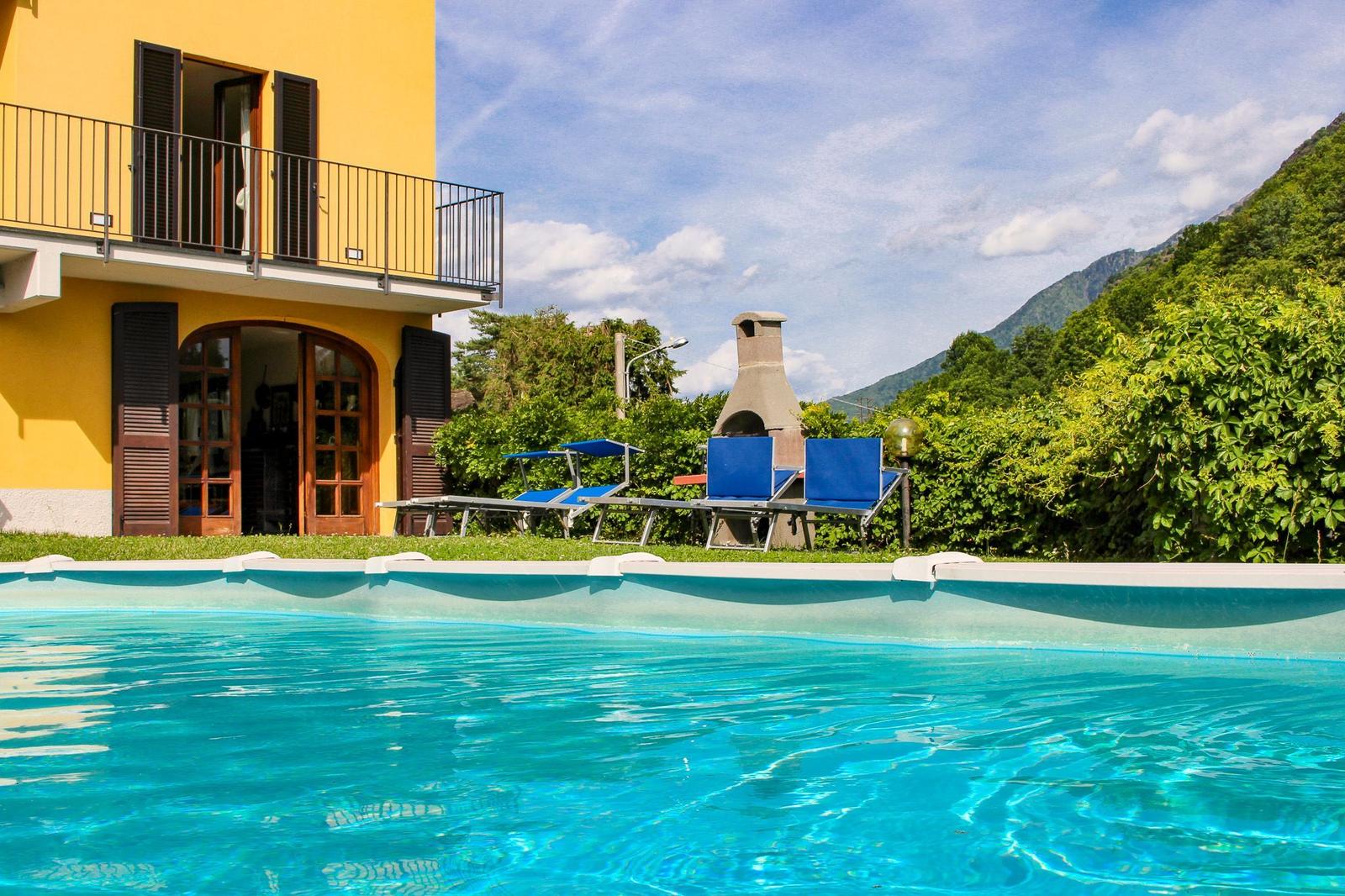 Pool mit Liegestühlen, Grill und gelbem Haus mit Balkon.