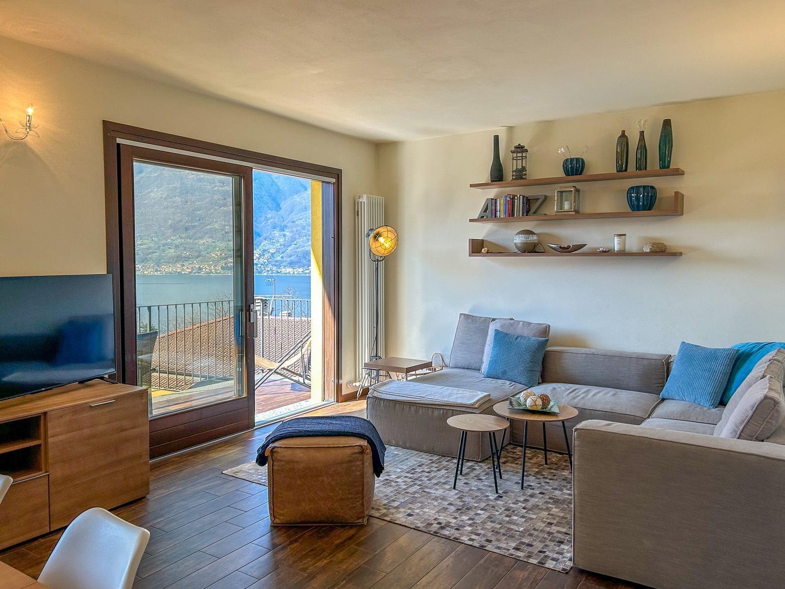 Wohnzimmer mit Sofa, TV und Balkonblick auf See und Berge.