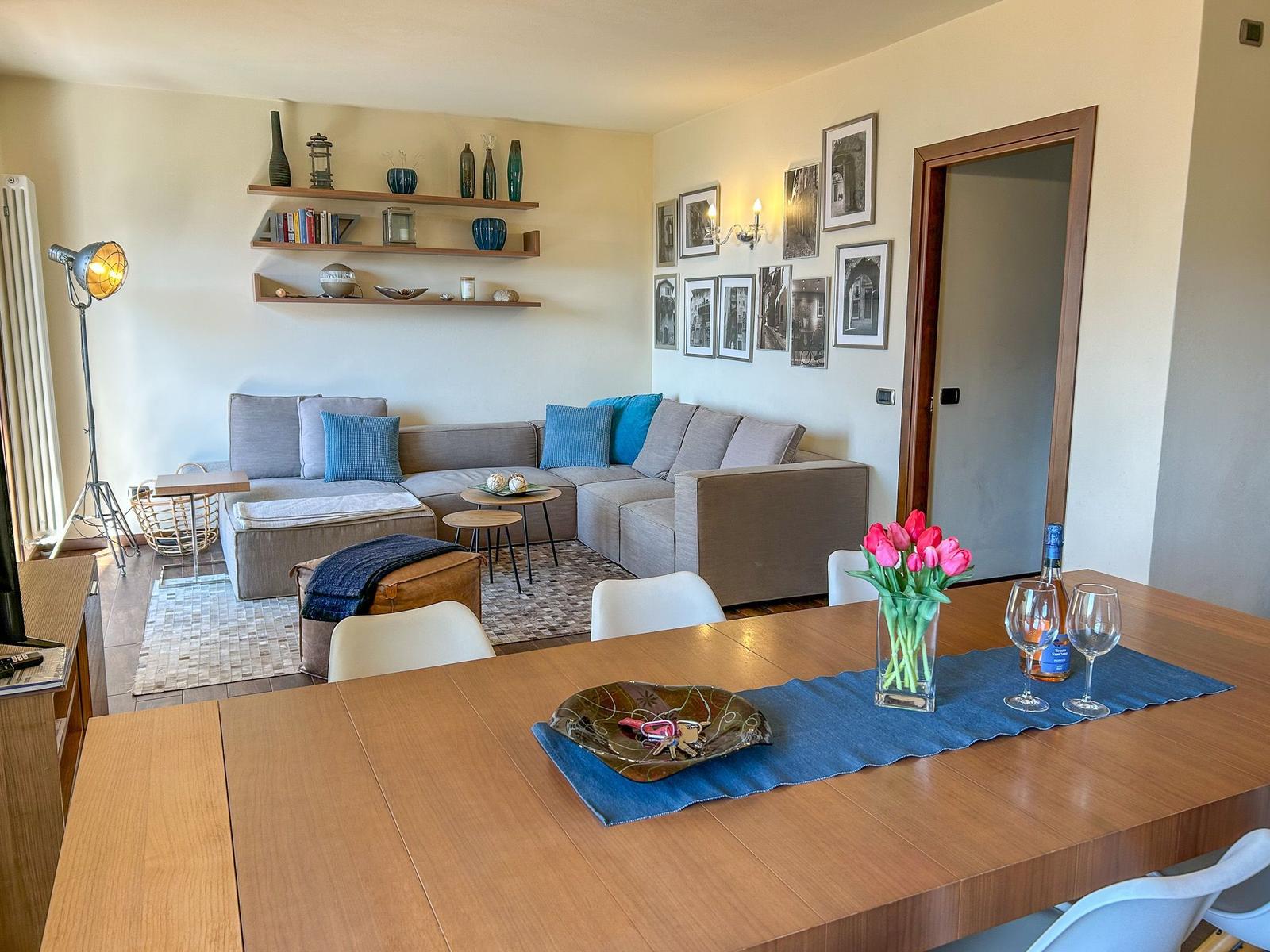 Ein Essbereich mit Tisch und Stühlen. Im Hintergrund ein Wohnbereich mit Sofa und Wandregalen.