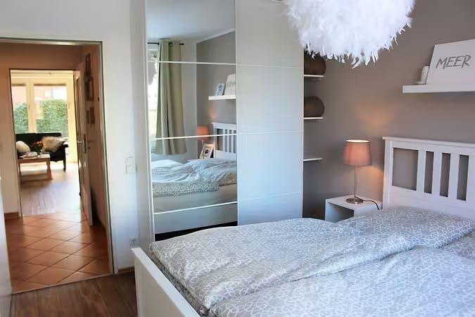 Schlafzimmer mit Spiegelschrank, Bett und Nachttisch. Durchgang zur Wohnfläche mit Sofa.