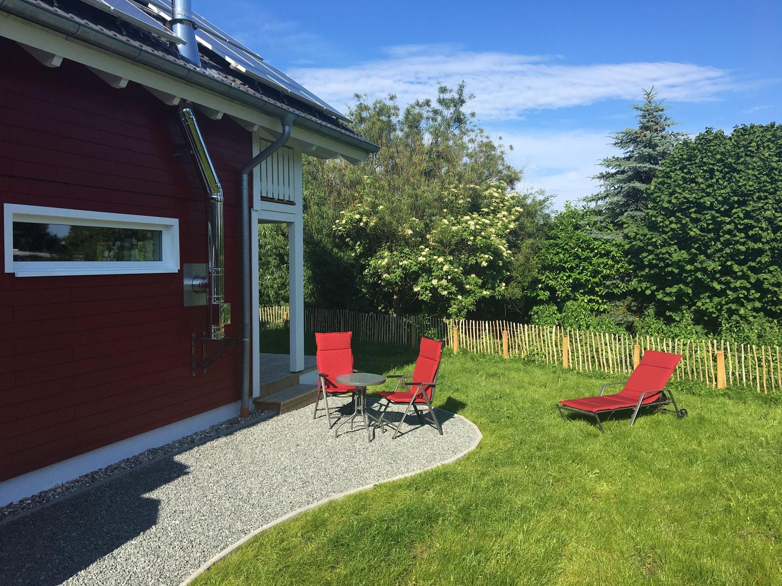 Roter Gartenbereich mit Liegestühlen und Tisch neben Haus.